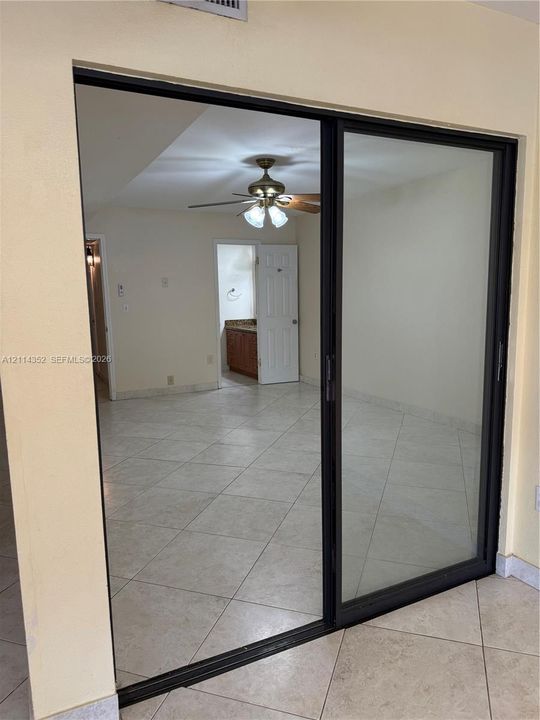 Large sliding glass door with a dark-finished frame, tile flooring, and a ceiling fan with integrated lighting