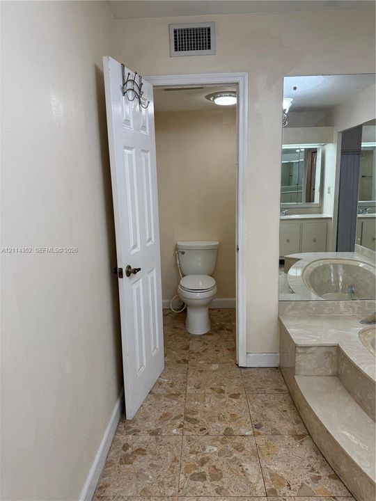 Bathroom featuring stone-finish tile flooring, a built-in recessed soaking tub with a stepped stone surround, and an expansive wall-to-wall mirror
