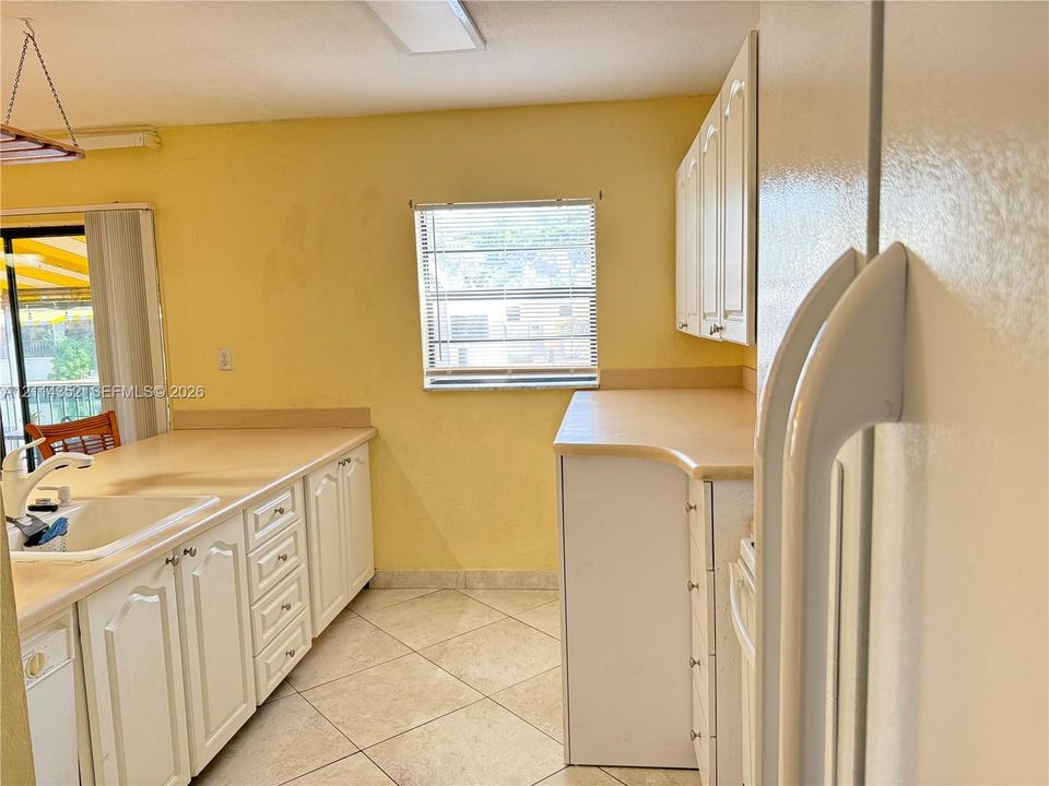 Kitchen featuring white shaker-style cabinetry, solid-surface countertops, a recessed double-basin sink, and ceramic tile flooring