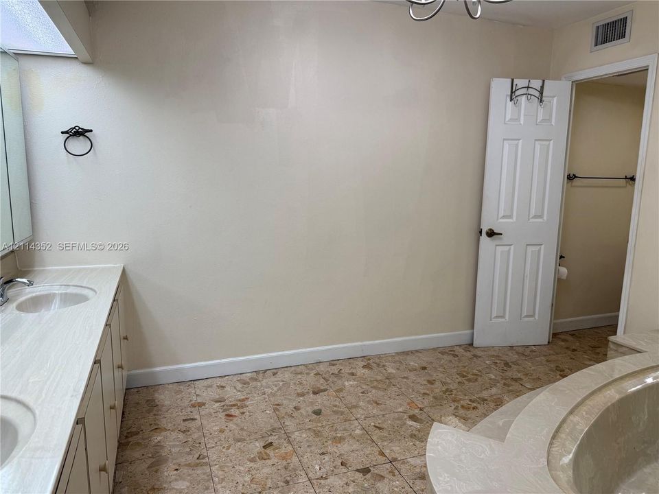 Bathroom featuring a dual-sink vanity with light-toned countertop, terrazzo-style tile flooring, and a raised platform soaking tub