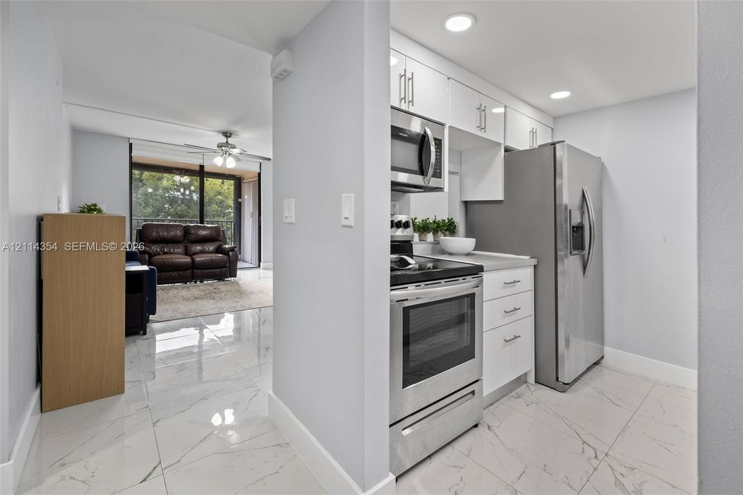 Kitchen featuring white cabinetry, stainless steel appliances, and solid surface countertops complemented by polished tile flooring with a veined pattern