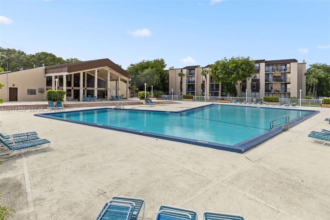Large swimming pool with a concrete pool deck, encompassing structure with a covered pavilion, and perimeter fencing
