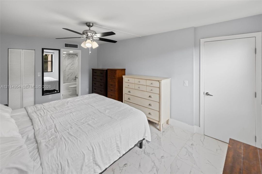 Interior space featuring stone-style tile flooring, multi-blade ceiling fan with integrated light fixture, dual louvered closet doors, and smooth-finish walls
