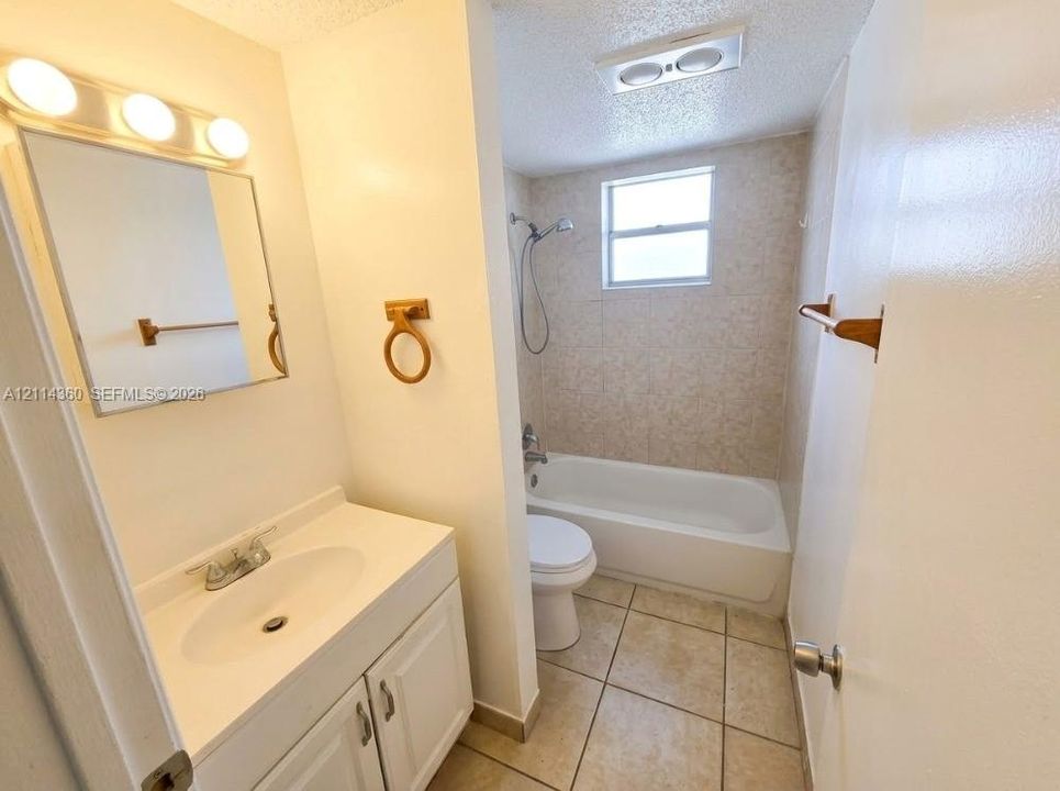 Bathroom featuring a white vanity with integrated sink, three-light wall-mounted fixture, tiled flooring, and a shower-tub combination with wall tiling