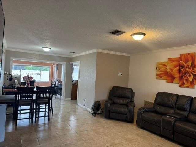 Open-concept living space featuring large-format ceramic tile flooring, neutral wall tones, crown molding, and dual flush-mount light fixtures