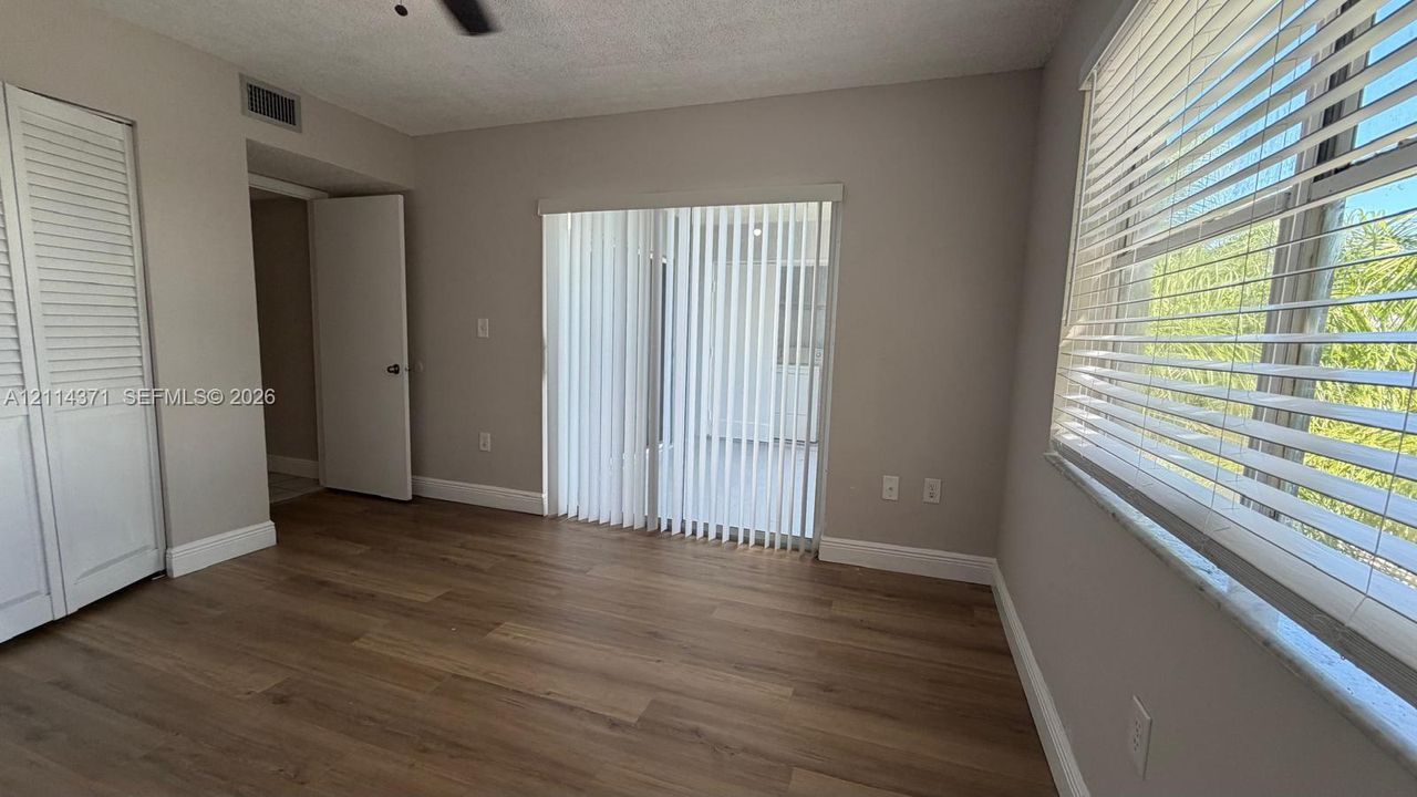 Wood-finish flooring, white louvered-door closet, ceiling fan, and sliding glass doors featuring vertical blinds