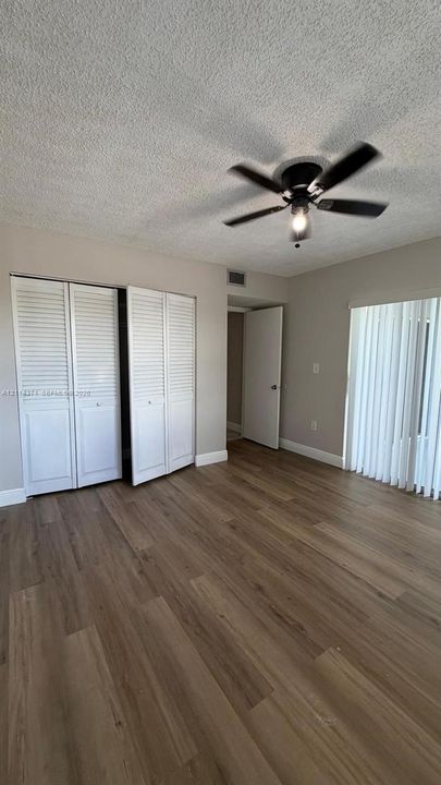 Room featuring wood-finish flooring, white louvered-panel closet doors, textured ceiling, central ceiling fan, and vertical blinds