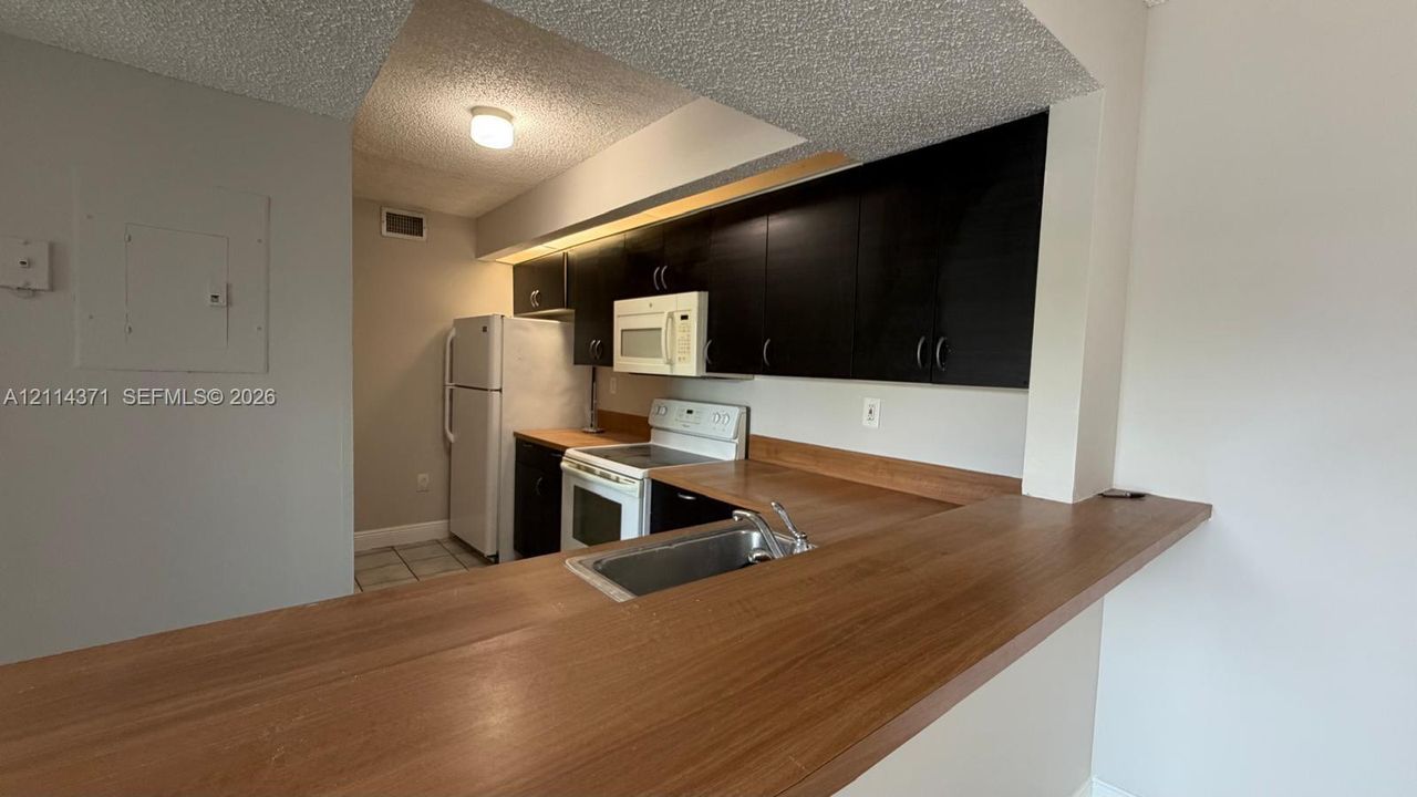 Kitchen featuring dark cabinetry, expansive wood-surface peninsula, integrated lighting, and white appliances