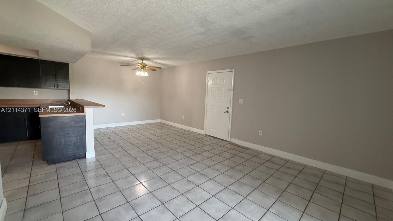 Open-concept interior featuring large-format ceramic floor tiling, dark cabinetry, wood-finish countertops, a breakfast bar, and a ceiling-mounted light fixture