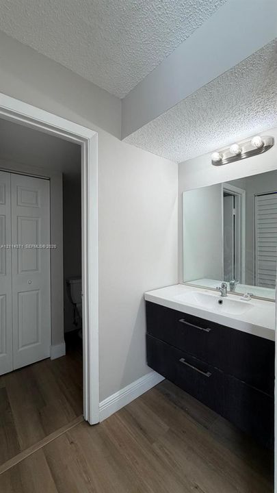 Floating vanity featuring two drawers, a rectangular integrated basin, and a chrome faucet, complemented by a large wall-mounted mirror and a three-bulb vanity light fixture