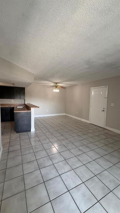 Open-concept interior featuring light-toned tile flooring, a kitchen peninsula with a countertop, dark-toned cabinetry, and a ceiling-mounted fan with integrated lighting