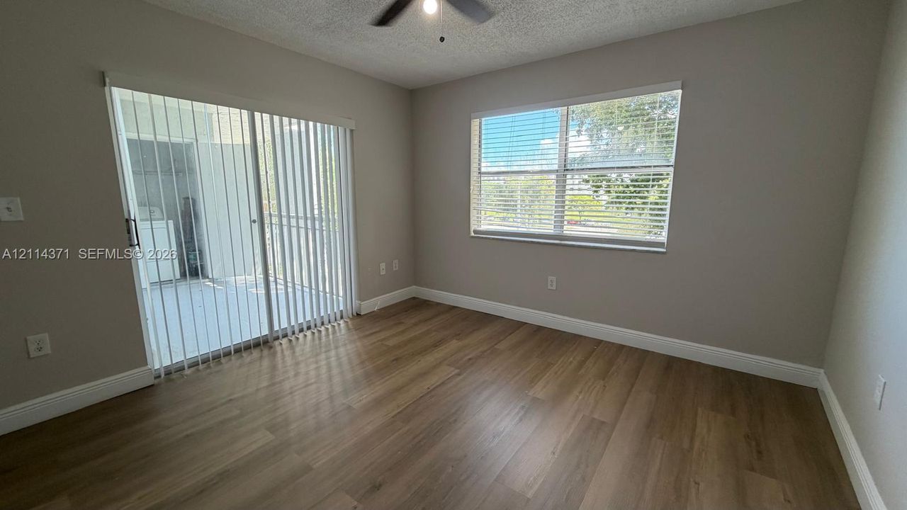 Neutral-toned interior featuring wood-finish flooring, a ceiling fan, a horizontal window with blinds, and sliding glass doors with vertical blinds
