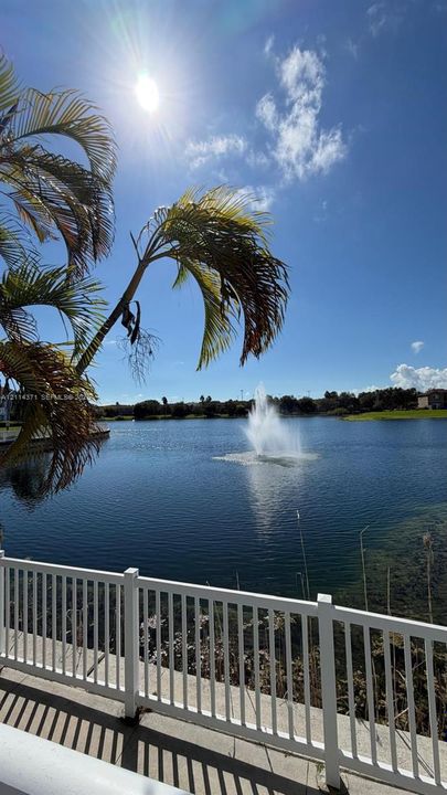 Waterfront property featuring a decorative fountain, white vinyl fencing, and mature palm trees