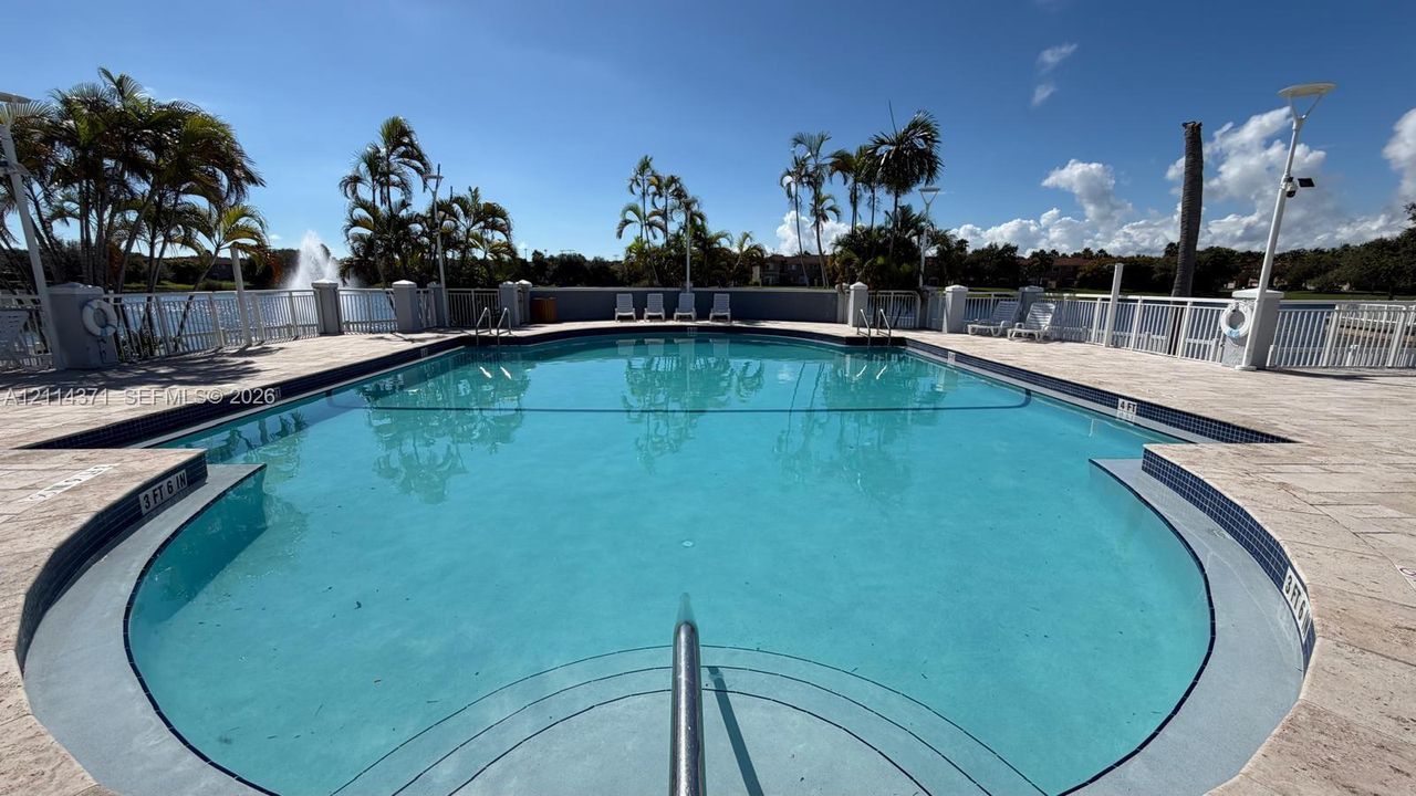 In-ground swimming pool with stone-tiled decking, integrated steps, a perimeter metal fence, and water fountain feature