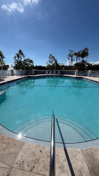 Swimming pool with integrated entry steps, metal handrail, and stone-tile pool deck, enclosed by a perimeter fence