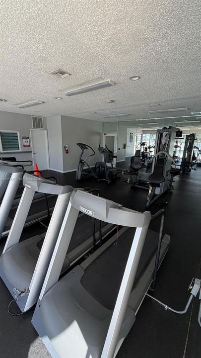 Fitness center featuring rubberized flooring, mirrored walls, and recessed fluorescent lighting