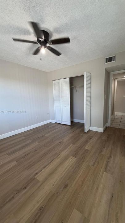 Wood-finish flooring, ceiling fan with integrated lighting, and closet with white louvered doors