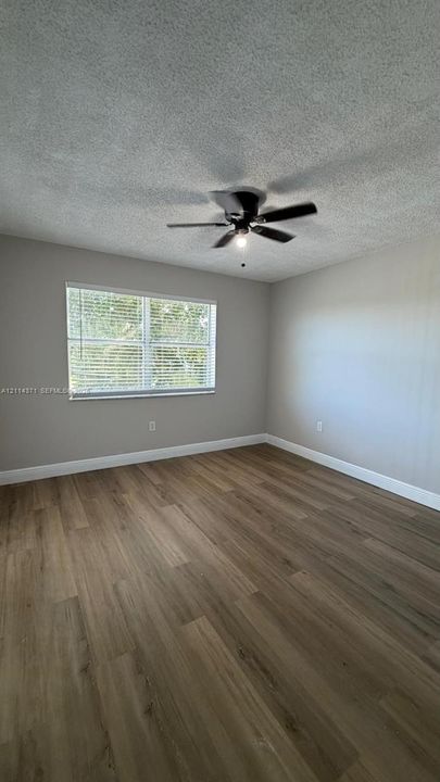 Room featuring wood-finish flooring, neutral wall paint, a multi-blade ceiling fan with integrated lighting, and a single-pane window