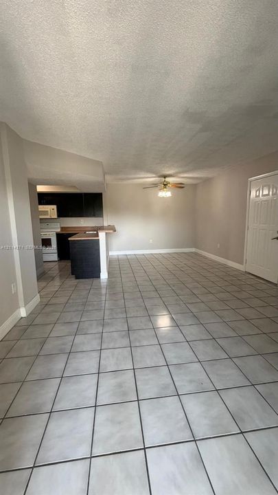 Open-concept interior featuring neutral tile flooring, a kitchen breakfast bar with dark cabinetry, and a ceiling fan with integrated lighting
