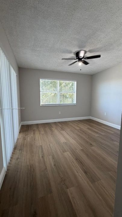 Interior space featuring wood-finish flooring, a ceiling fan with integrated lighting, neutral wall paint, and vertical blinds