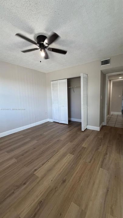 Wood-finish flooring, ceiling fan, and closet featuring white louvered doors