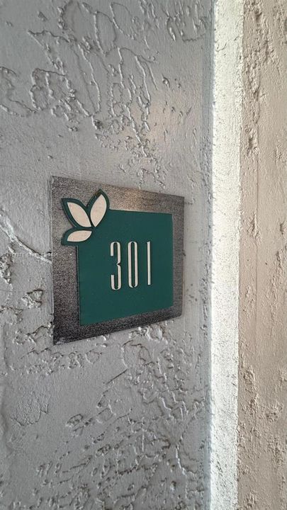 Custom unit signage featuring metallic backing, a teal accent panel, and decorative leaf detailing, mounted on a textured stucco wall