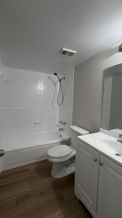 Bathroom featuring a white vanity cabinet with a integrated sink, wood-finish flooring, and a shower-tub combination with a wall-mounted handheld fixture