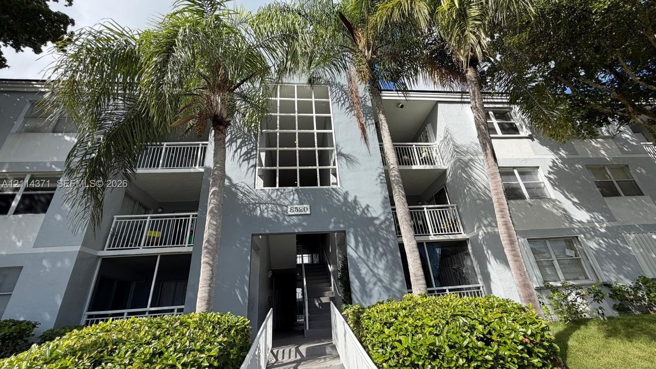 Multi-story exterior featuring a grid-patterned architectural window, private balconies with vertical railings, and mature palm trees