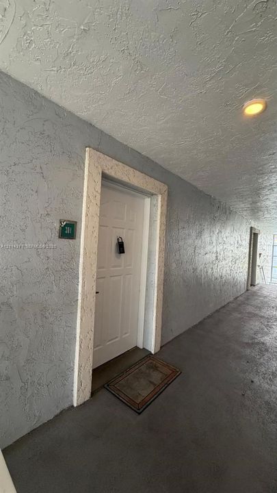 White paneled entrance door featuring a decorative textured surround, set against a light grey stucco exterior wall with recessed ceiling lighting