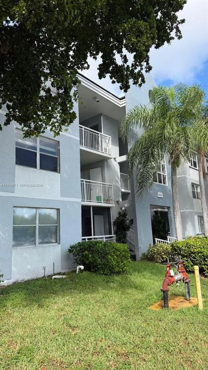 Multi-story stucco exterior featuring stacked balconies with metal railings, horizontal window configurations, and mature palm landscaping