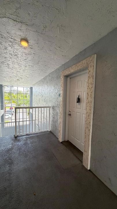Exterior landing featuring a six-panel door with stone-finish trim, textured stucco walls, overhead flush-mount lighting, and a white metal safety railing