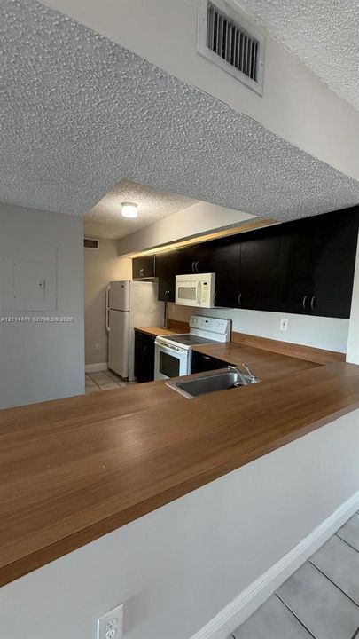Kitchen featuring dark cabinetry, expansive wood-finish countertops, integrated under-cabinet lighting, and tile flooring