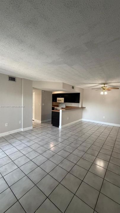 Open-concept living space featuring large-format ceramic tile flooring, a kitchen breakfast bar, dark-toned cabinetry, and a ceiling-mounted fan