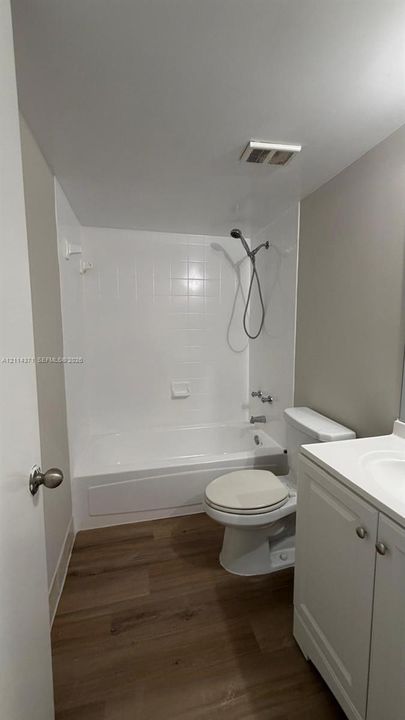 Bathroom featuring wood-finish flooring, white vanity cabinet with a neutral countertop, and a shower-tub combination with white tile surround and a handheld shower fixture