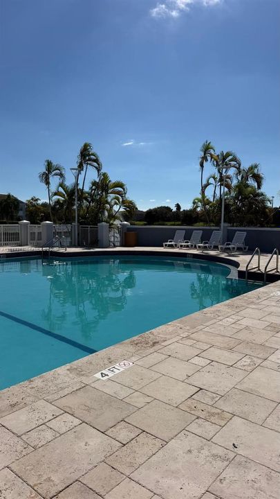 Swimming pool with stone-tiled decking, perimeter fencing, and mature palm trees