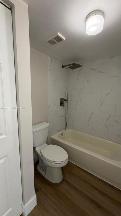 Bathroom featuring large-format wall tile with a veined pattern, a square shower head, a handheld shower attachment, and wood-finish flooring