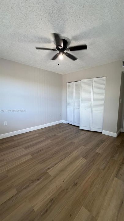 Room featuring wood-finish flooring, textured ceiling, central ceiling fan, and white louvered-panel closet doors
