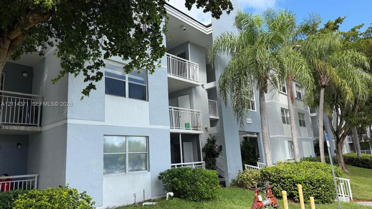 Multi-story exterior featuring light-toned stucco siding, private balconies with metal railings, and screened patio enclosures