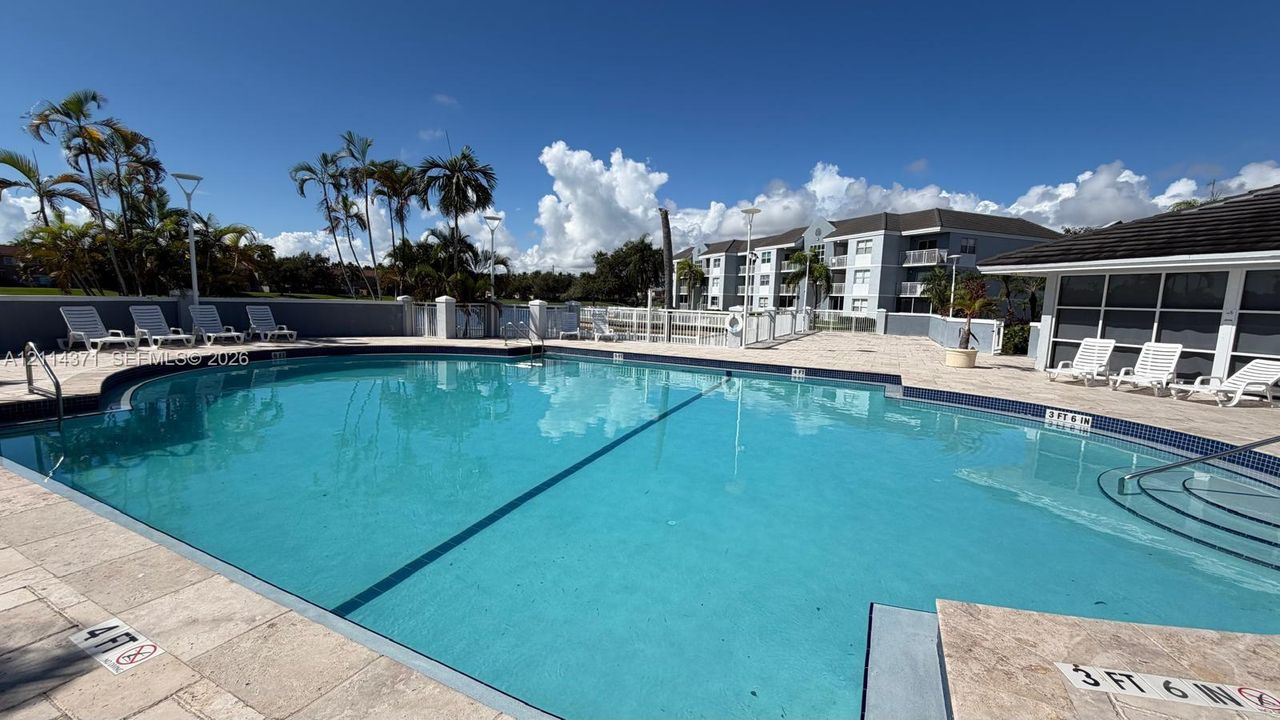 Community pool featuring a curved concrete basin, stone-tile decking, built-in stair entry, and perimeter fencing