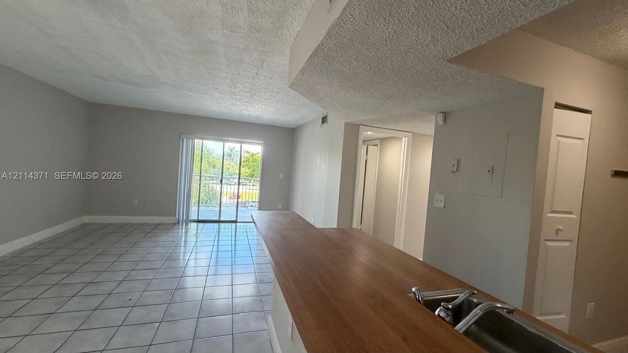 Open-concept floor plan featuring ceramic tile flooring, a breakfast bar with a wood-finish countertop, stainless steel dual-basin sink, and a glass sliding door