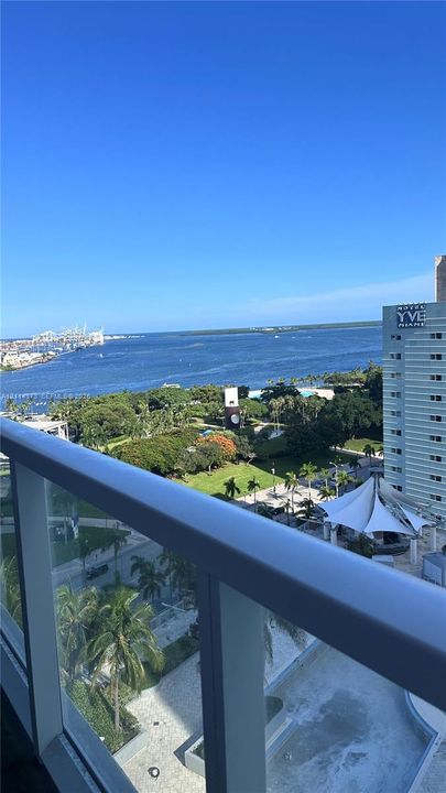 Balcony featuring a metal and glass railing, overlooking an expansive urban waterfront and park area