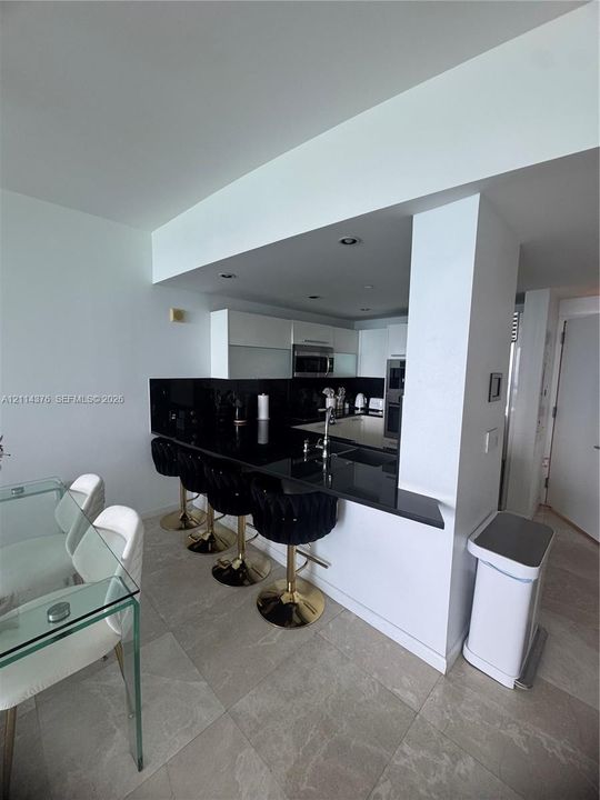 Kitchen featuring dark stone-surface breakfast bar, recessed ceiling lighting, flat-panel cabinetry, stainless steel appliances, and stone-finish flooring