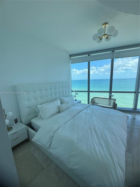 Floor-to-ceiling windows featuring ocean scenery, tile flooring, and a modern multi-globe chandelier