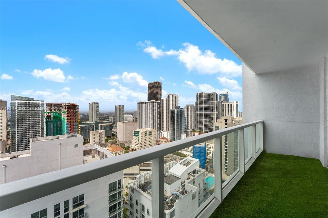 Covered balcony featuring artificial turf flooring and a glass railing