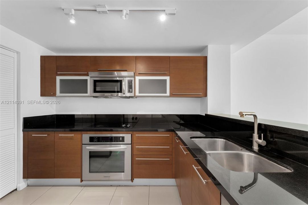 Kitchen featuring dark wood-finish cabinetry, stainless steel appliances, black stone countertops, double-basin stainless steel sink, and track lighting