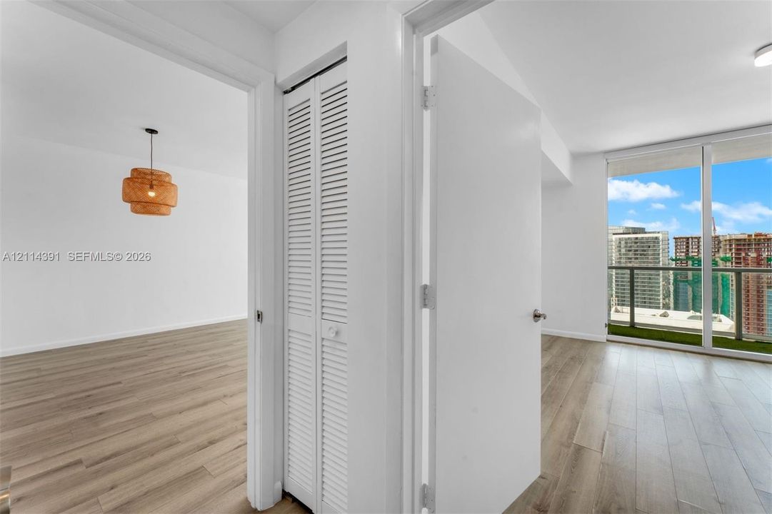 Wood-finish flooring, floor-to-ceiling glass windows, louvered bi-fold closet doors, and a private balcony featuring a metal railing