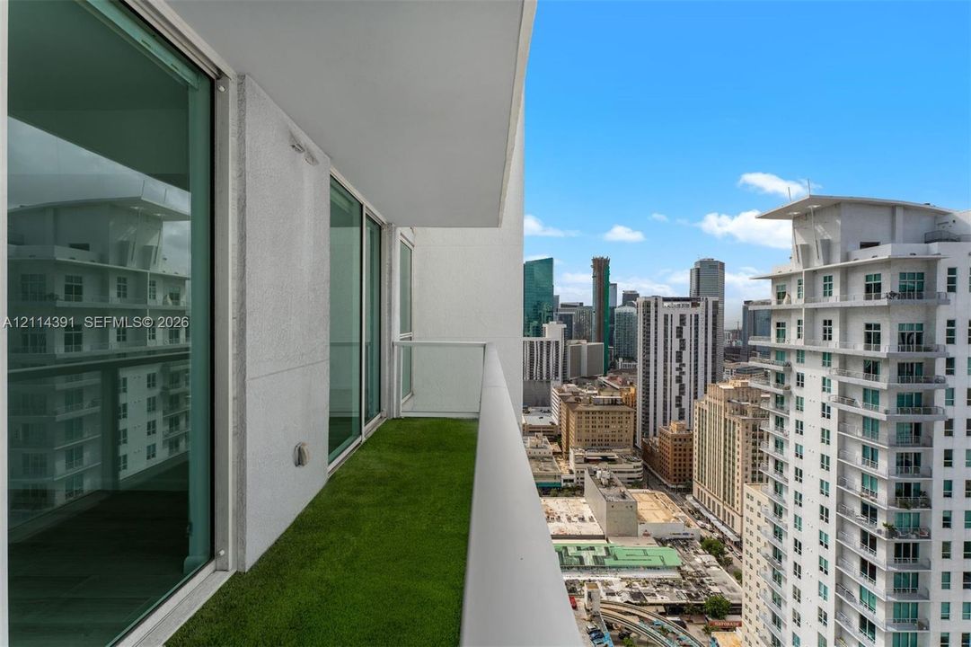 Private balcony featuring artificial turf flooring, floor-to-ceiling glass sliding doors, and a glass panel railing