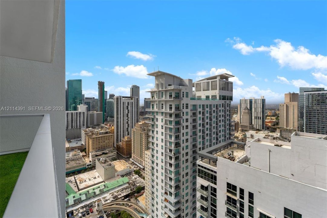 Private balcony with green turf surfacing and metal railings overlooking the high-density urban cityscape