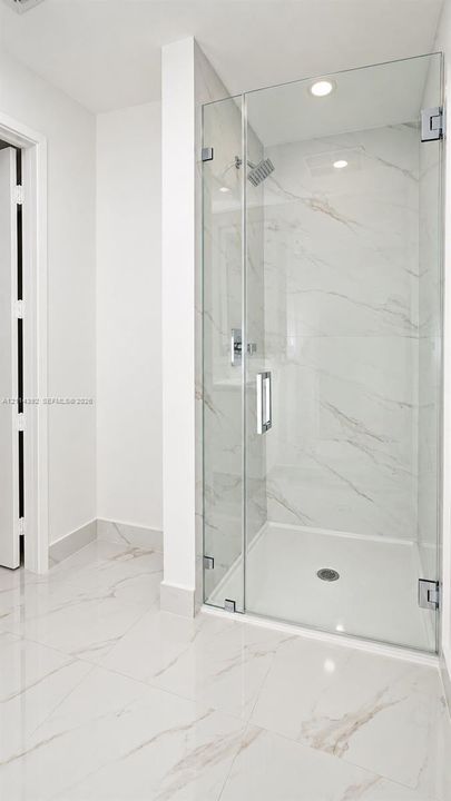 Walk-in shower featuring glass enclosure, wall-mounted rainfall showerhead, and large-format tile flooring and wall surfacing with veined detailing