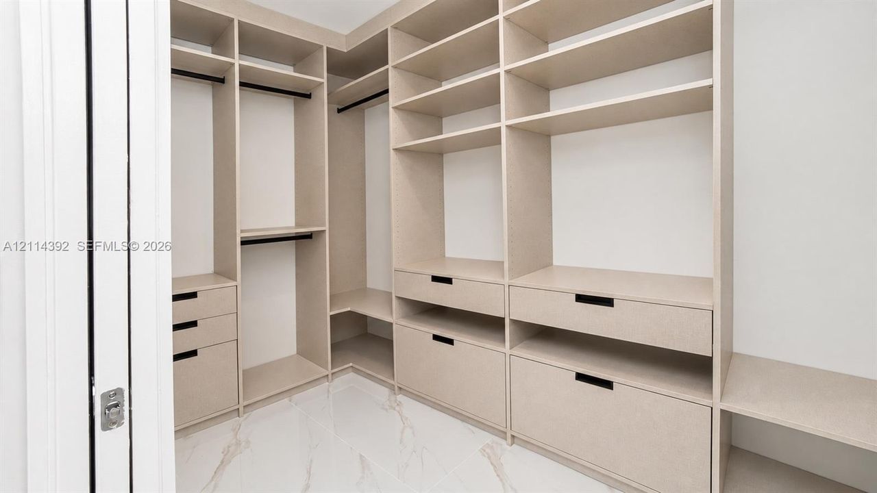Custom walk-in closet featuring extensive built-in shelving, integrated storage drawers, hanging rods, and large-format tile flooring